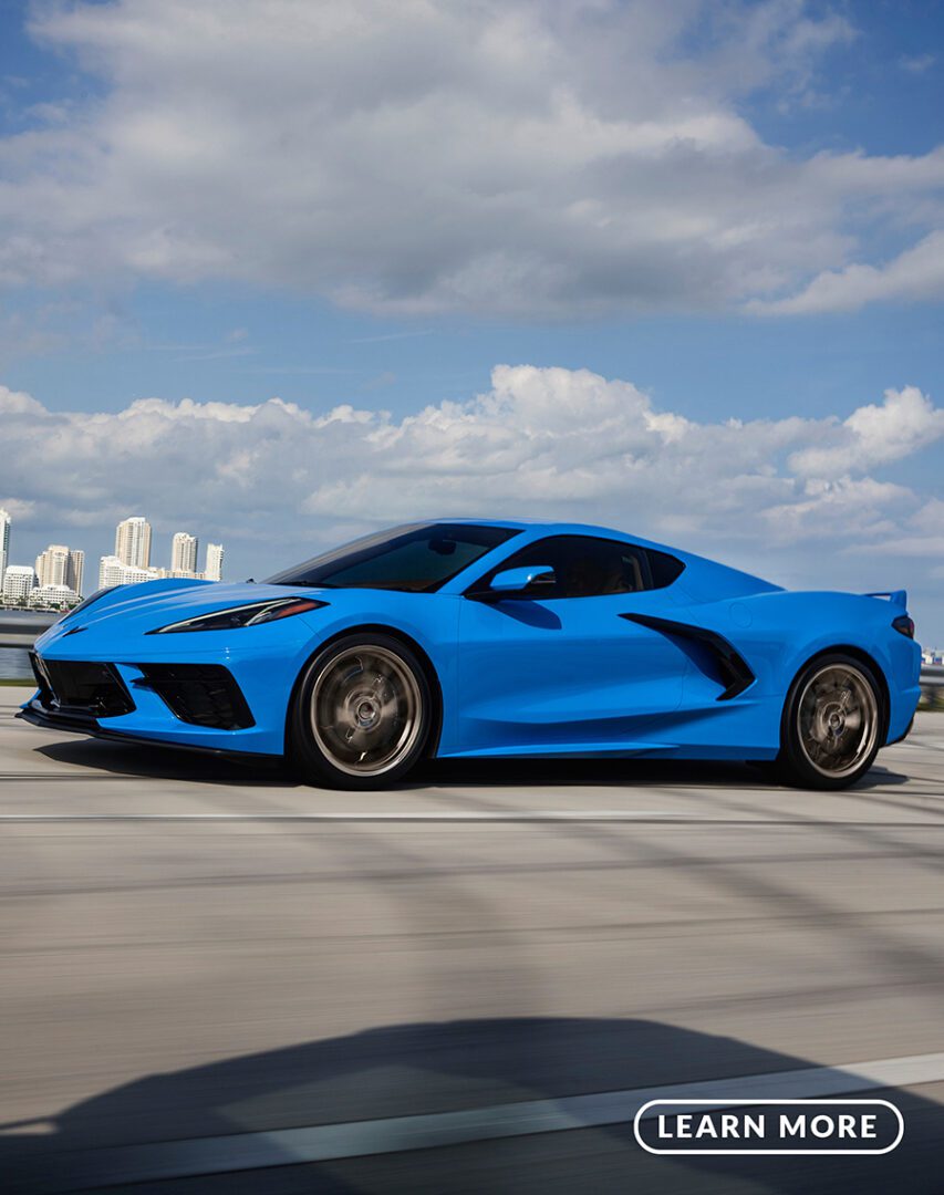A blue chevrolet corvette stingray driving on a road.