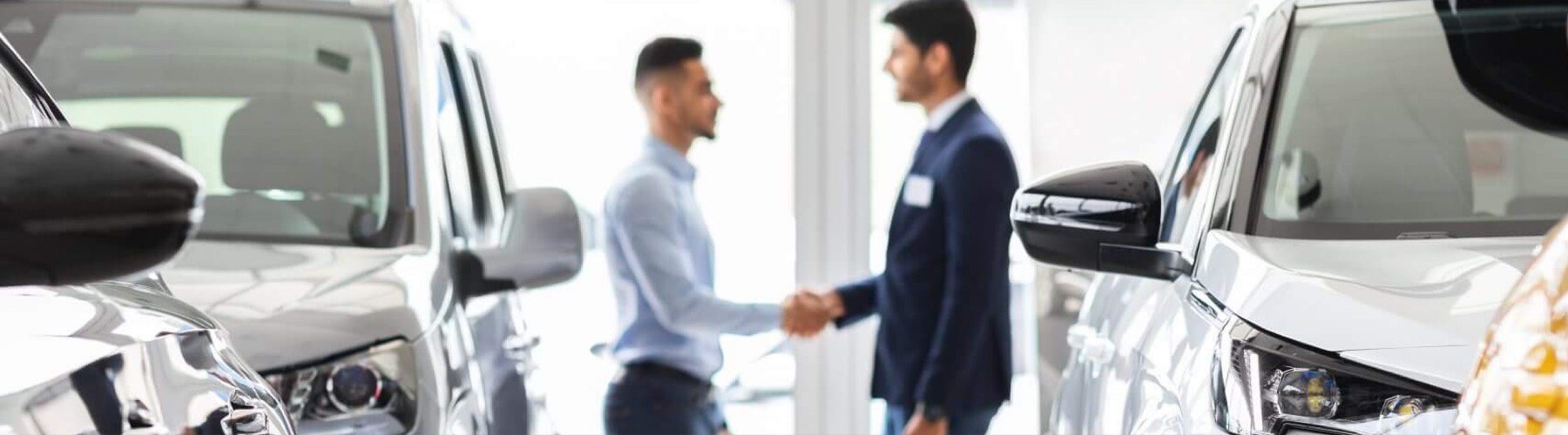 Two men shaking hands in a car showroom.