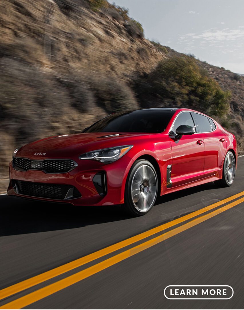 A red kia sting driving down a mountain road.
