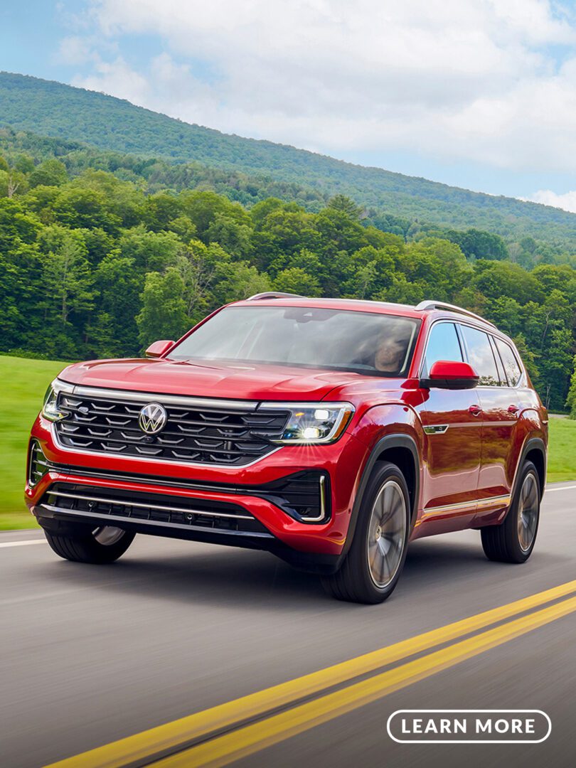 A red volkswagen atlas driving down a country road.